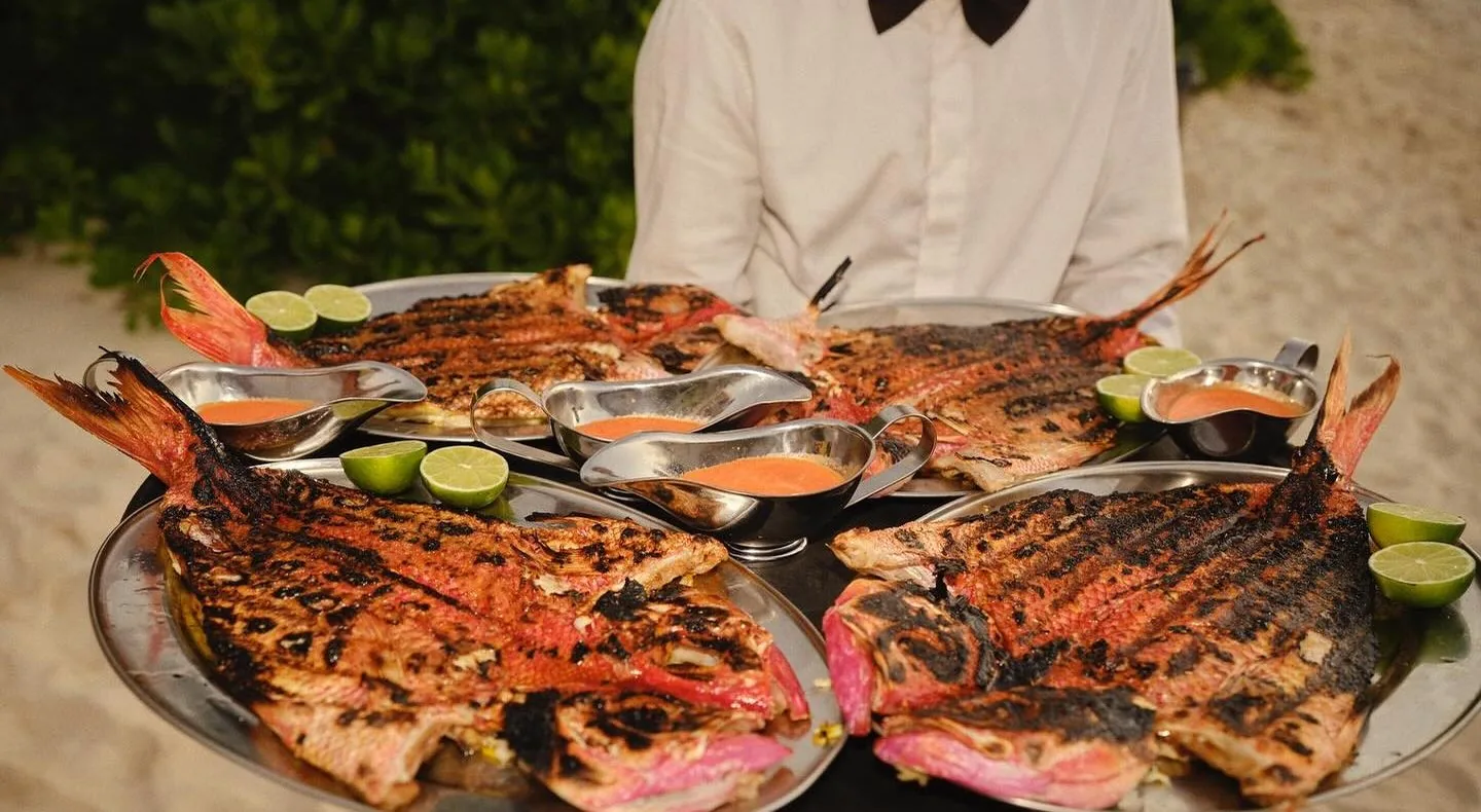 Server carrying trays of whole grilled snapper at a beachside 305 Catering dinner